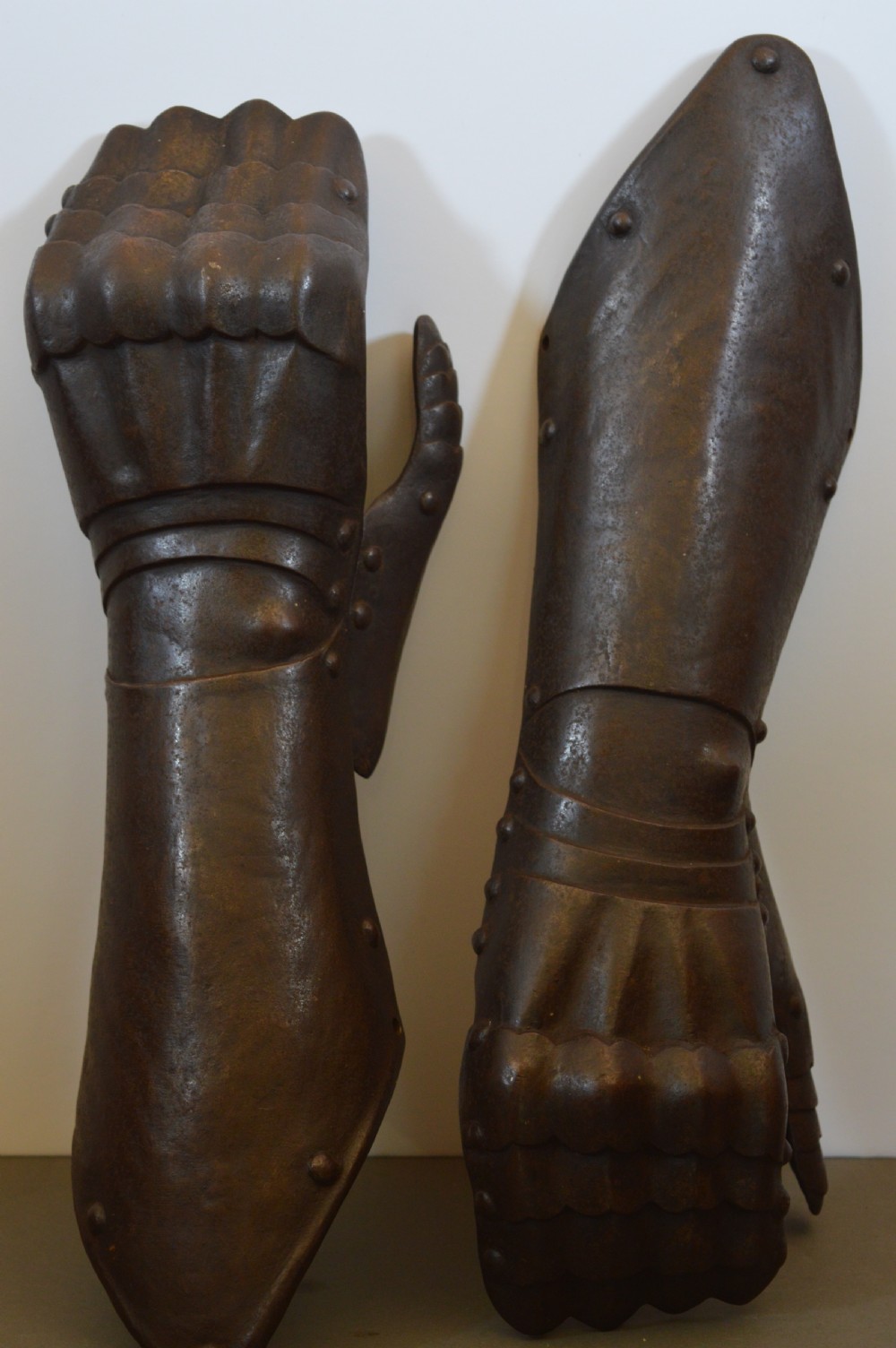 A pair of 19th-century articulated iron armour gauntlets with layered finger plates, flared cuffs, and visible rivets with an oxidised patina. View II