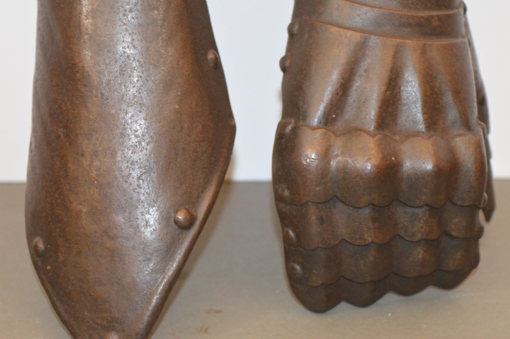 A pair of 19th-century articulated iron armour gauntlets with layered finger plates, flared cuffs, and visible rivets with an oxidised patina. View VI
