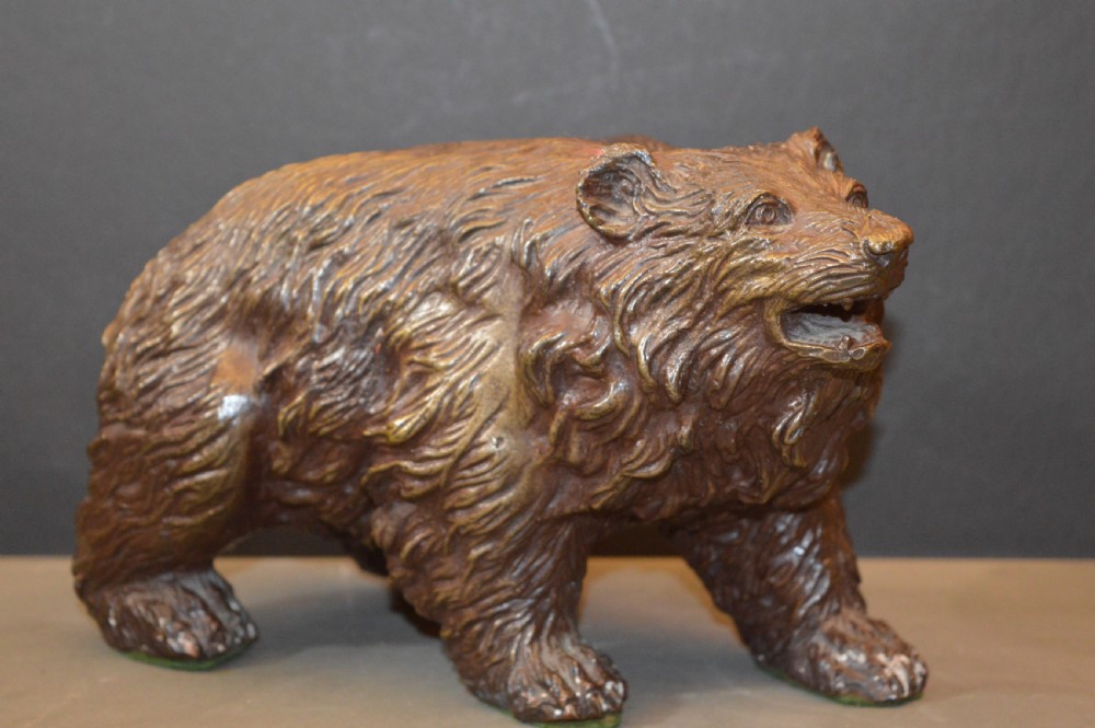A heavy cast bronze sculpture depicting a bear with textured fur and an open mouth in a walking pose.