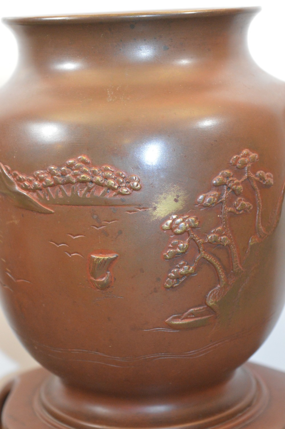 A Japanese Meiji period bronze urn featuring low relief carvings of pine trees and mountains with twin handles, resting on a matching carved bronze tripod stand. View II
