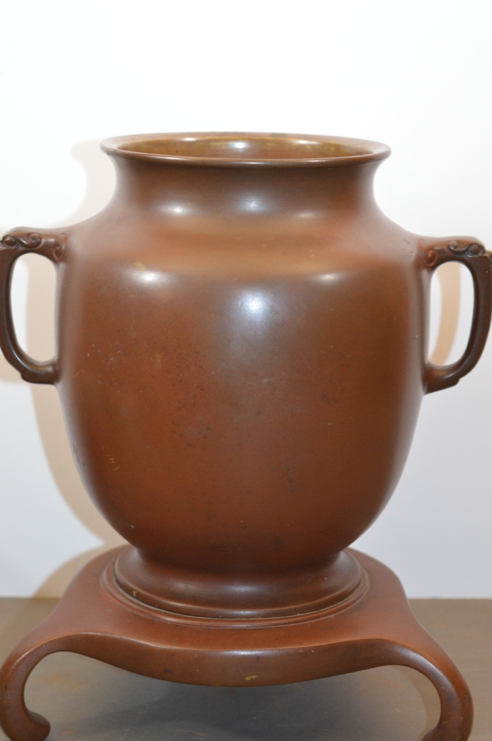 A Japanese Meiji period bronze urn featuring low relief carvings of pine trees and mountains with twin handles, resting on a matching carved bronze tripod stand. View V