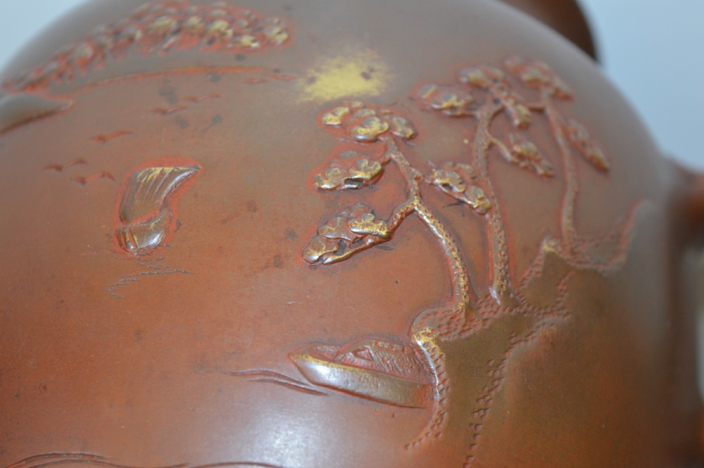 A Japanese Meiji period bronze urn featuring low relief carvings of pine trees and mountains with twin handles, resting on a matching carved bronze tripod stand. View VIII