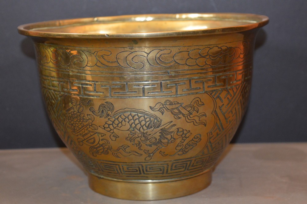 A heavy polished brass Japanese jardiniere with incised dragon artwork and geometric key fret borders around the exterior.