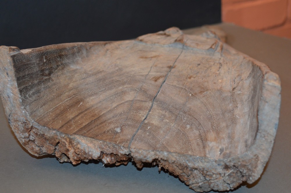A carved wooden canoe prow shaped like a stylised crocodile head with weathered grey timber and incised geometric details around the eyes. View V