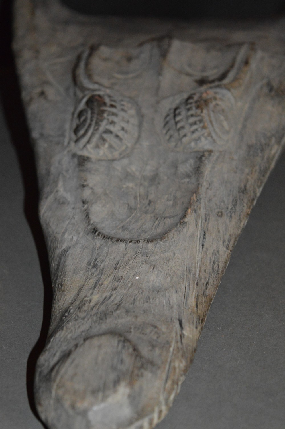 A carved wooden canoe prow shaped like a stylised crocodile head with weathered grey timber and incised geometric details around the eyes. View XI
