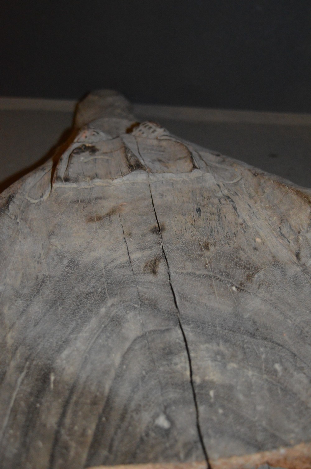 A carved wooden canoe prow shaped like a stylised crocodile head with weathered grey timber and incised geometric details around the eyes. View XV