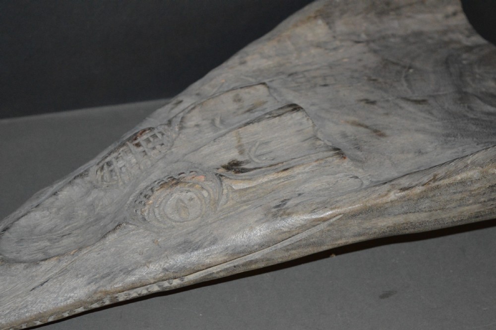 A carved wooden canoe prow shaped like a stylised crocodile head with weathered grey timber and incised geometric details around the eyes. View XIX