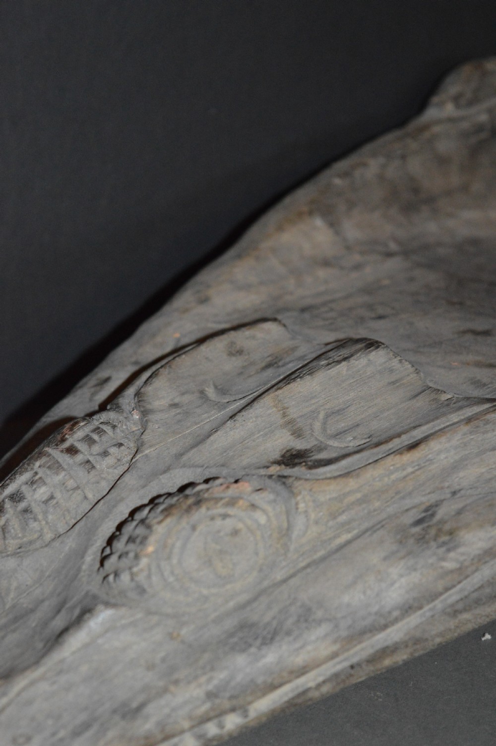 A carved wooden canoe prow shaped like a stylised crocodile head with weathered grey timber and incised geometric details around the eyes. View XX