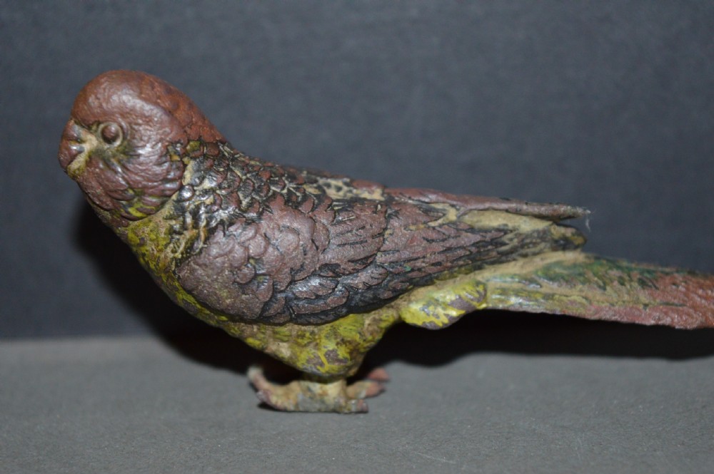 A cold-painted bronze figurine depicting a parrot with textured feather details in shades of brown, green, and yellow.