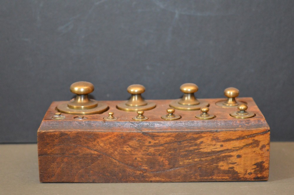 A rectangular wooden block stand fitted with a set of brass apothecary knobbed weights arranged by size.