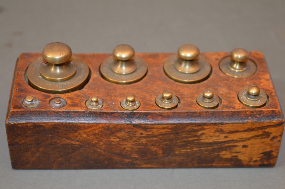 A rectangular wooden block stand fitted with a set of brass apothecary knobbed weights arranged by size. View III