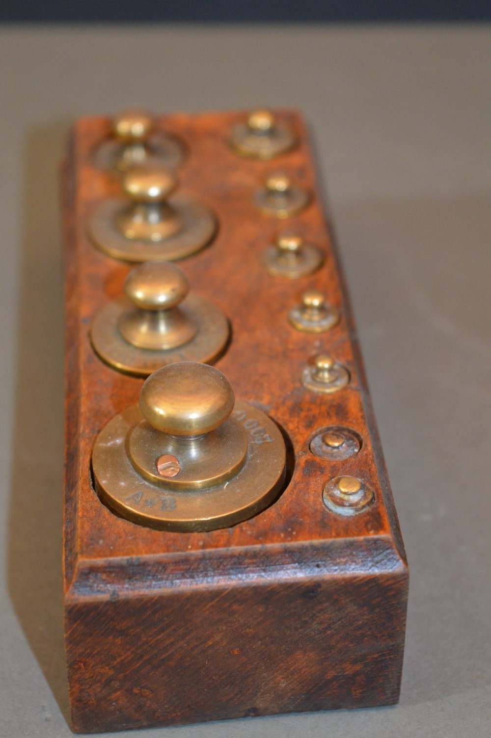 A rectangular wooden block stand fitted with a set of brass apothecary knobbed weights arranged by size. View IV