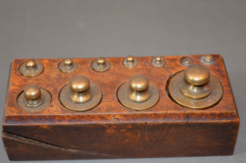 A rectangular wooden block stand fitted with a set of brass apothecary knobbed weights arranged by size. View V