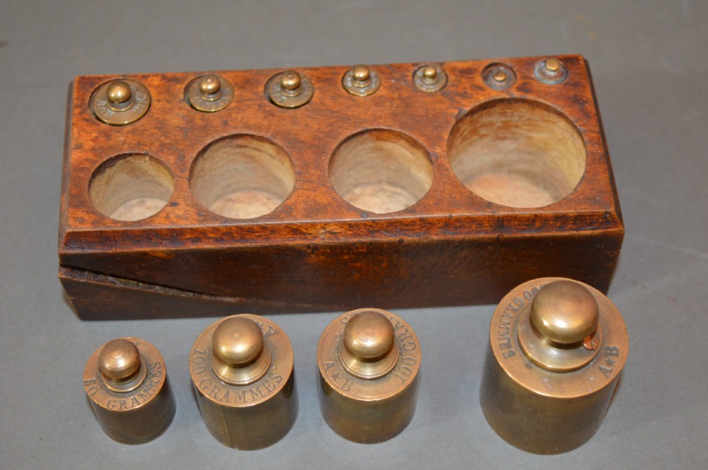 A rectangular wooden block stand fitted with a set of brass apothecary knobbed weights arranged by size. View VI