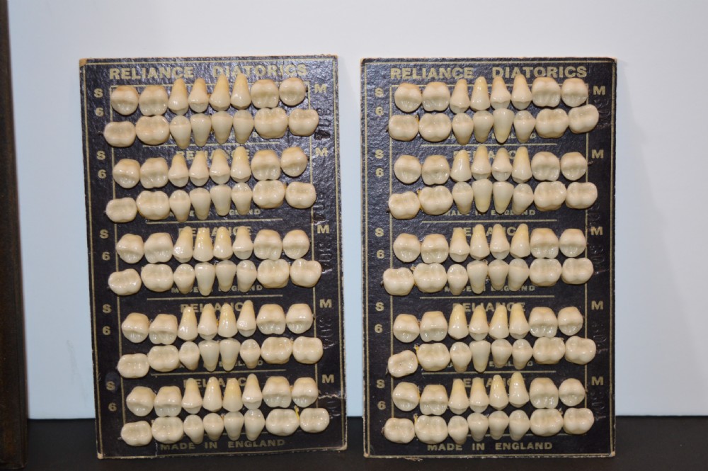 An antique framed copper dentist trade sign inscribed with business details alongside tooth sample cards and metal dental trays. View IV