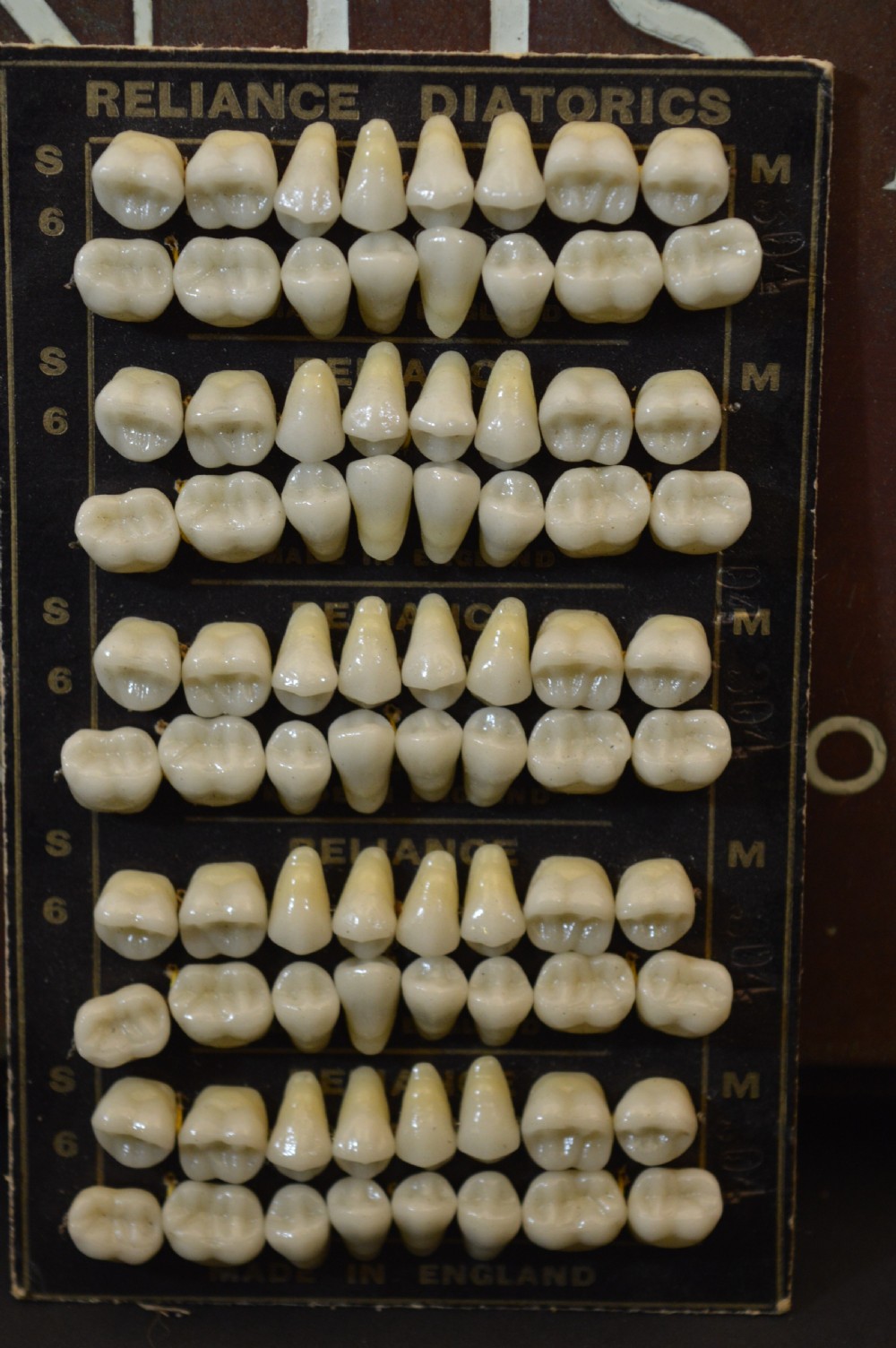An antique framed copper dentist trade sign inscribed with business details alongside tooth sample cards and metal dental trays. View IX