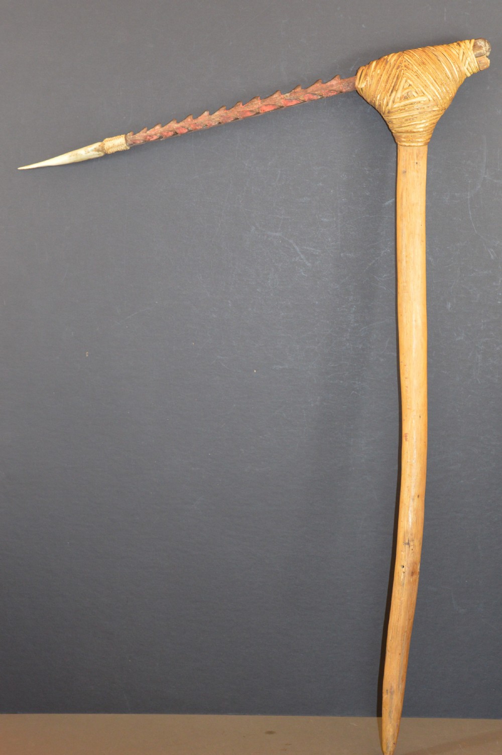 An antique Papua New Guinea fighting club featuring a angled wooden shaft, intricate woven rattan lashing, and a projecting serrated spike.