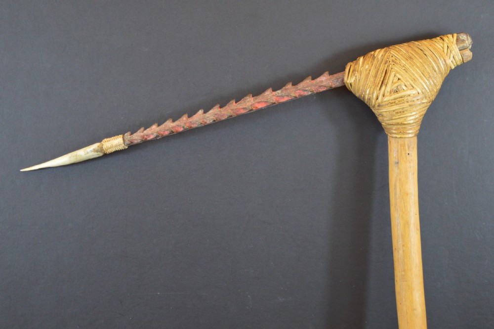 An antique Papua New Guinea fighting club featuring a angled wooden shaft, intricate woven rattan lashing, and a projecting serrated spike. View III