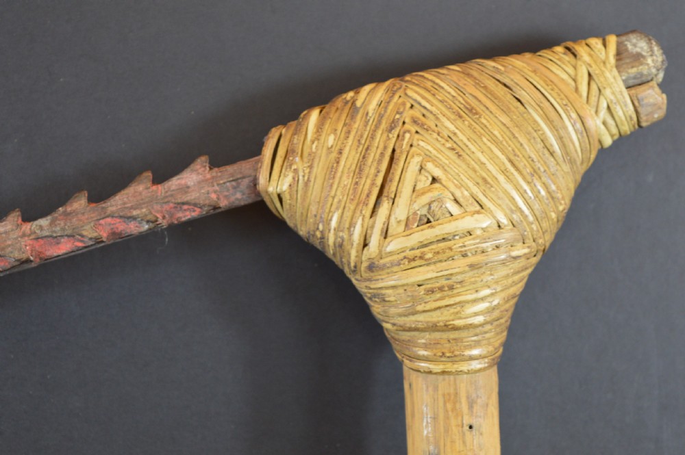An antique Papua New Guinea fighting club featuring a angled wooden shaft, intricate woven rattan lashing, and a projecting serrated spike. View V