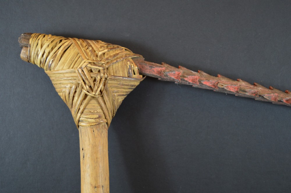 An antique Papua New Guinea fighting club featuring a angled wooden shaft, intricate woven rattan lashing, and a projecting serrated spike. View XI