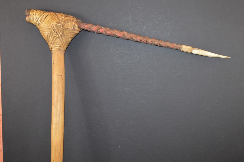 An antique Papua New Guinea fighting club featuring a angled wooden shaft, intricate woven rattan lashing, and a projecting serrated spike. View XIV