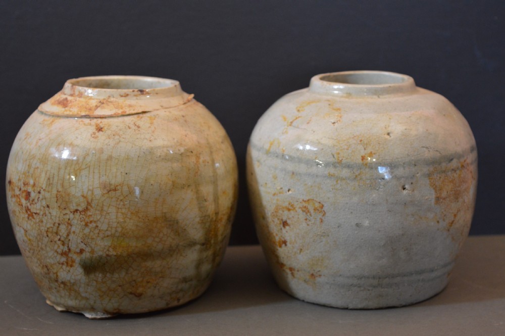 A pair of antique Chinese Ming dynasty ceramic pots featuring short rolled rims, globose bodies, and heavily crackled, patinated cream glazes.