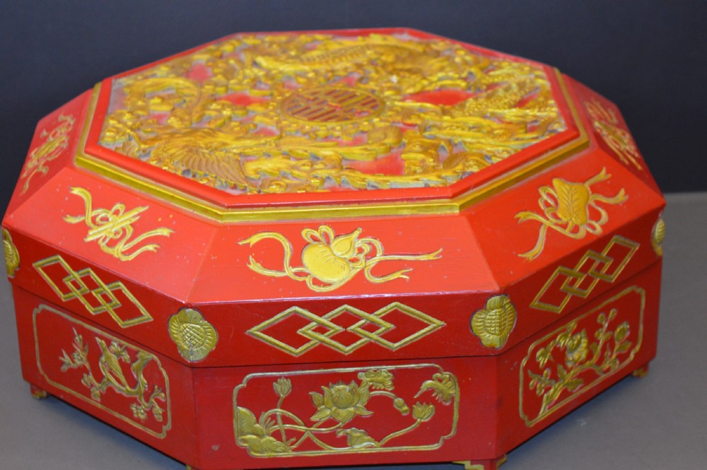 An octagonal Chinese red lacquer wedding box with relief-carved gold dragon and lotus motifs.