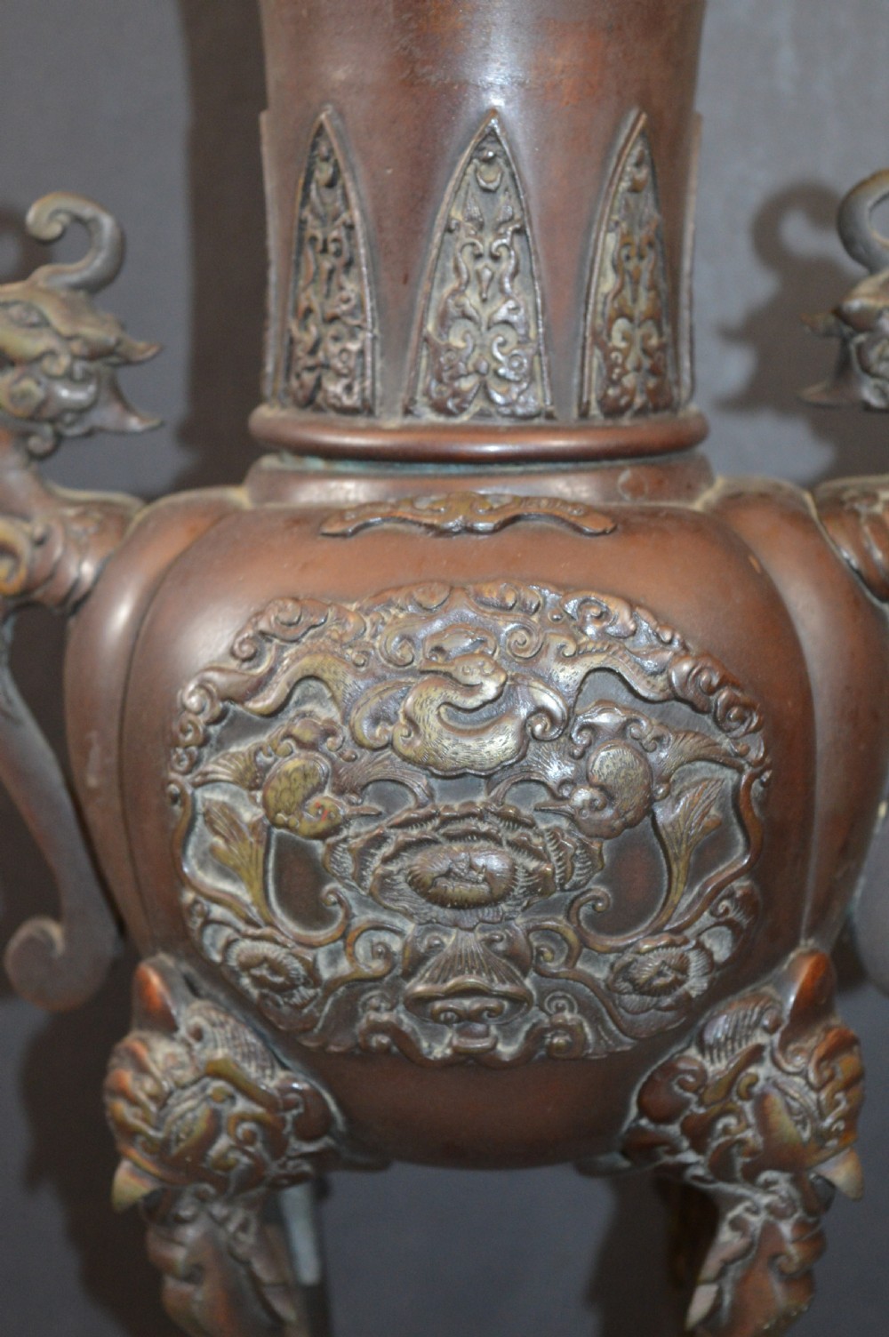 A heavy dark brown bronze Chinese incense burner featuring sculpted dragon handles, relief-carved medallions, and tall cabriole legs mounted on a round stand. View II
