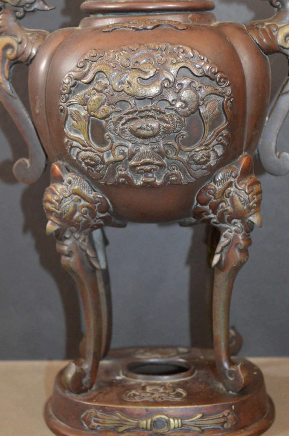 A heavy dark brown bronze Chinese incense burner featuring sculpted dragon handles, relief-carved medallions, and tall cabriole legs mounted on a round stand. View III