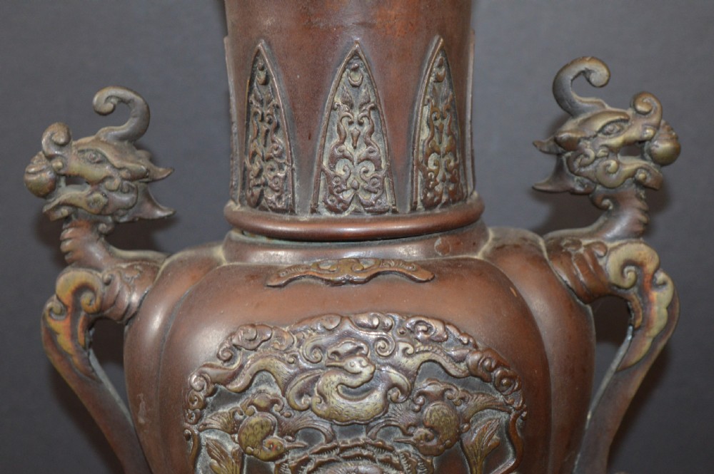 A heavy dark brown bronze Chinese incense burner featuring sculpted dragon handles, relief-carved medallions, and tall cabriole legs mounted on a round stand. View IV