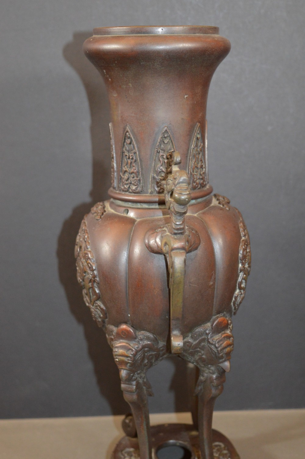 A heavy dark brown bronze Chinese incense burner featuring sculpted dragon handles, relief-carved medallions, and tall cabriole legs mounted on a round stand. View VI