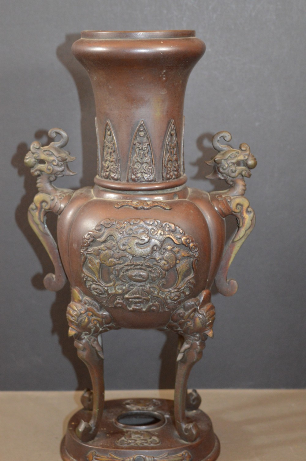 A heavy dark brown bronze Chinese incense burner featuring sculpted dragon handles, relief-carved medallions, and tall cabriole legs mounted on a round stand. View VII