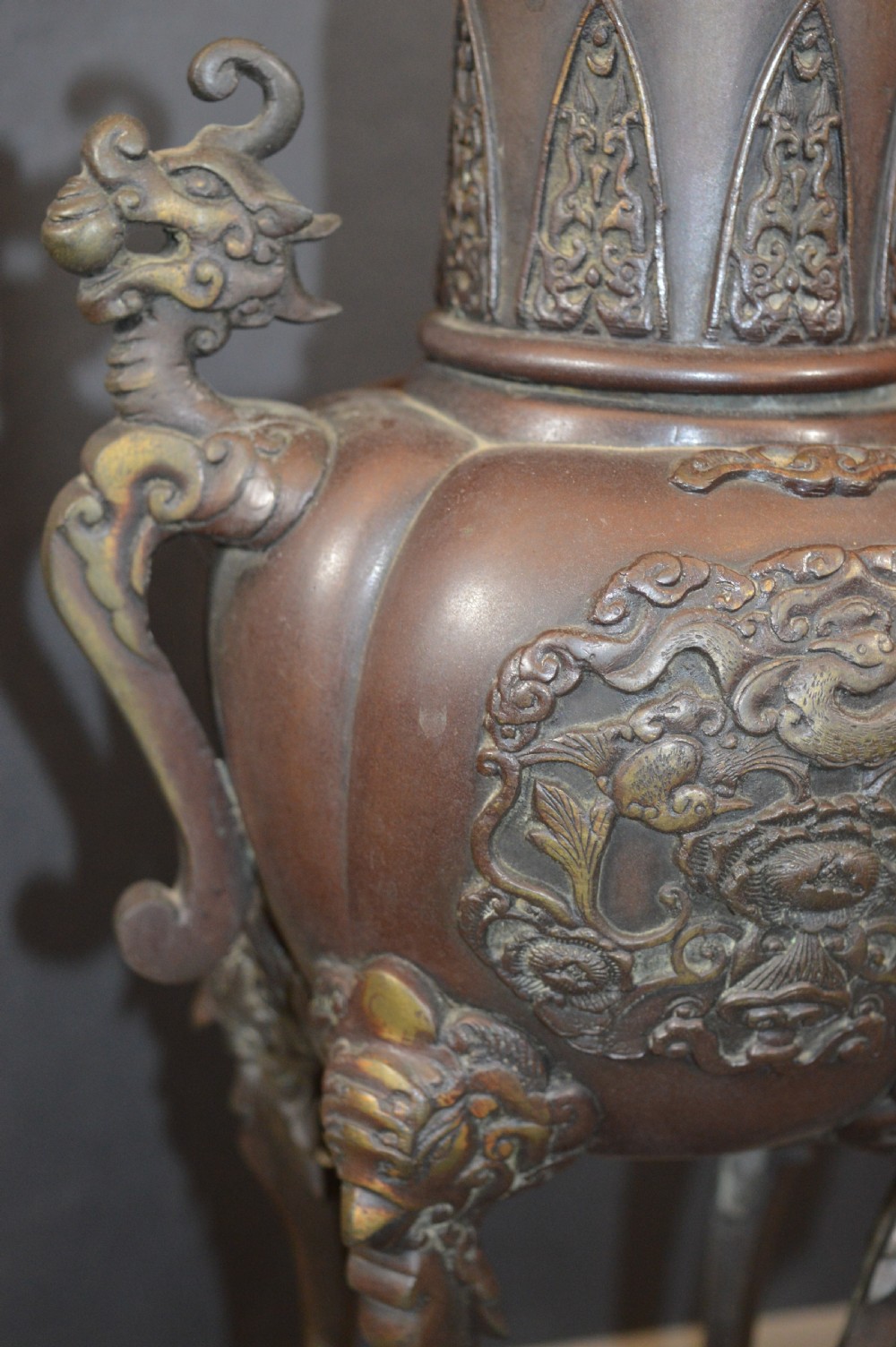 A heavy dark brown bronze Chinese incense burner featuring sculpted dragon handles, relief-carved medallions, and tall cabriole legs mounted on a round stand. View VIII