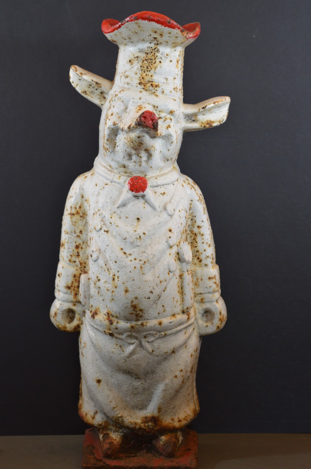 A late 19th-century cast iron figure of a pig dressed in butcher attire with distressed white paint and visible surface oxidisation.