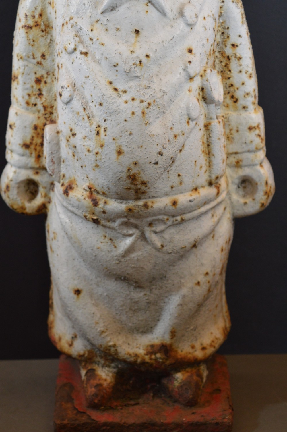 A late 19th-century cast iron figure of a pig dressed in butcher attire with distressed white paint and visible surface oxidisation. View III