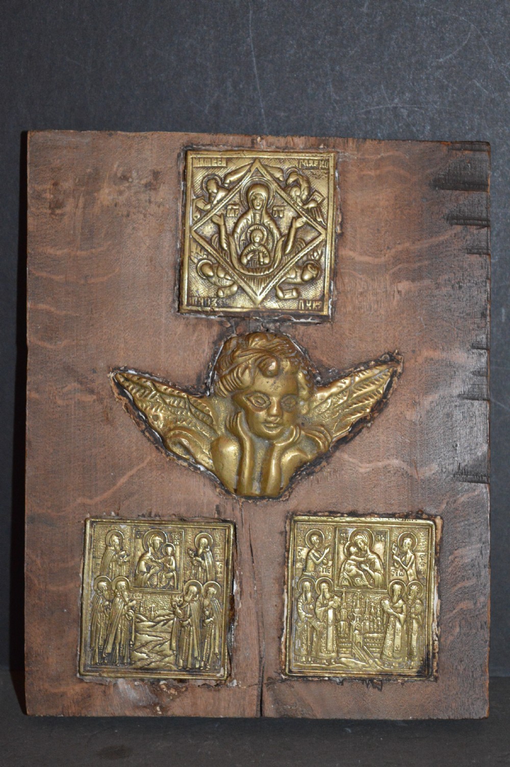 A rectangular wooden panel featuring three square brass Russian icons and a central relief of a winged angel head.