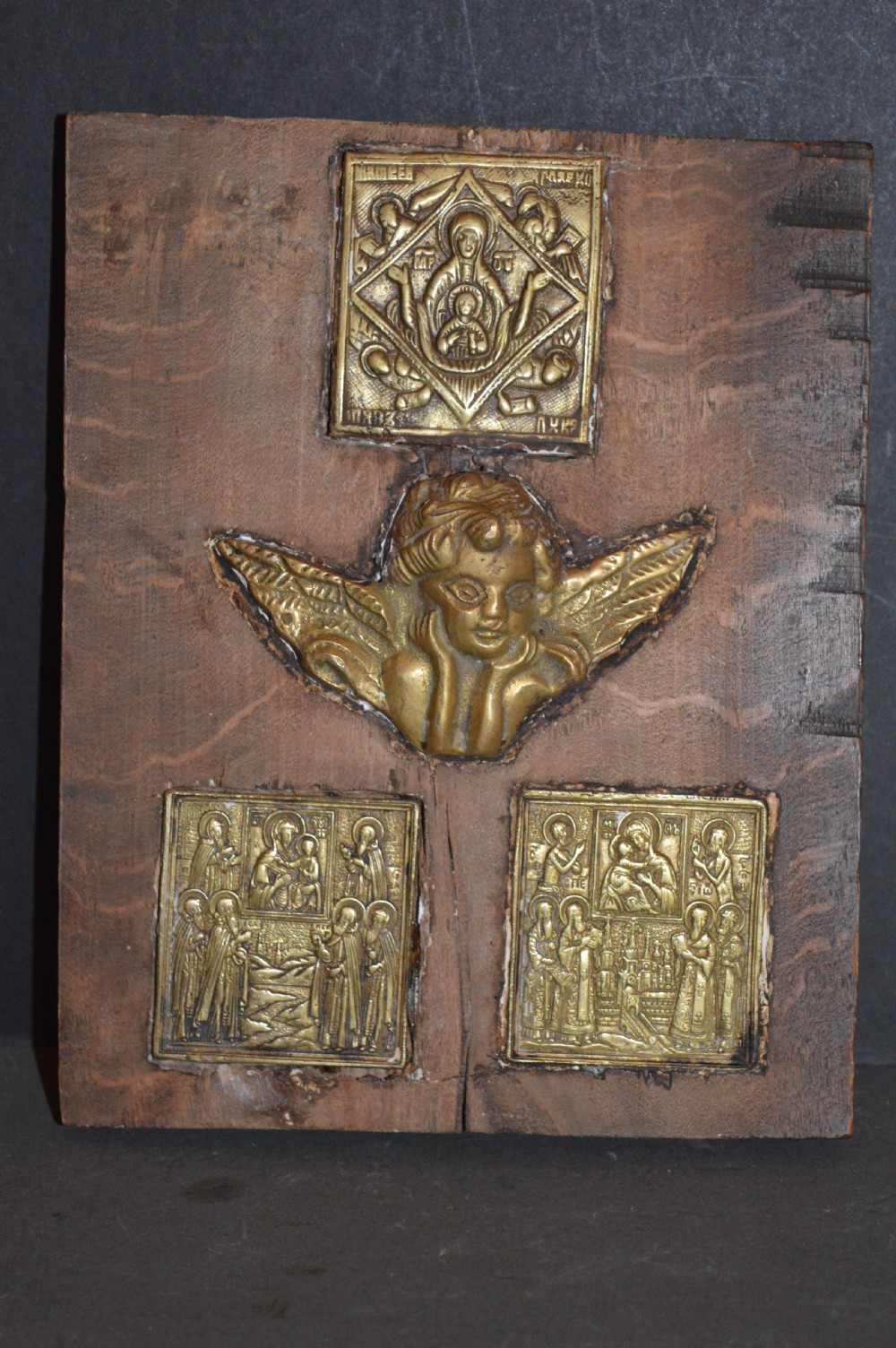 A rectangular wooden panel featuring three square brass Russian icons and a central relief of a winged angel head. View II
