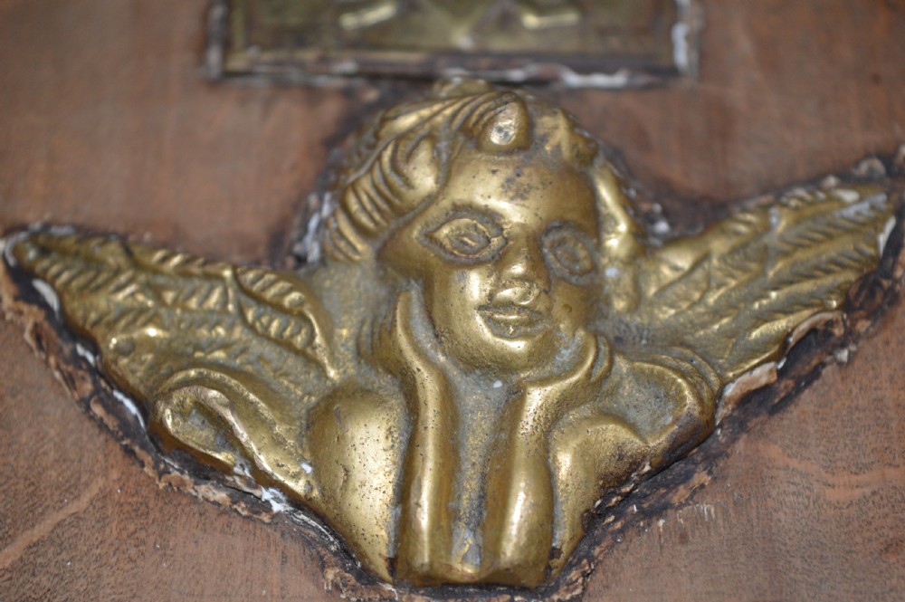 A rectangular wooden panel featuring three square brass Russian icons and a central relief of a winged angel head. View VII