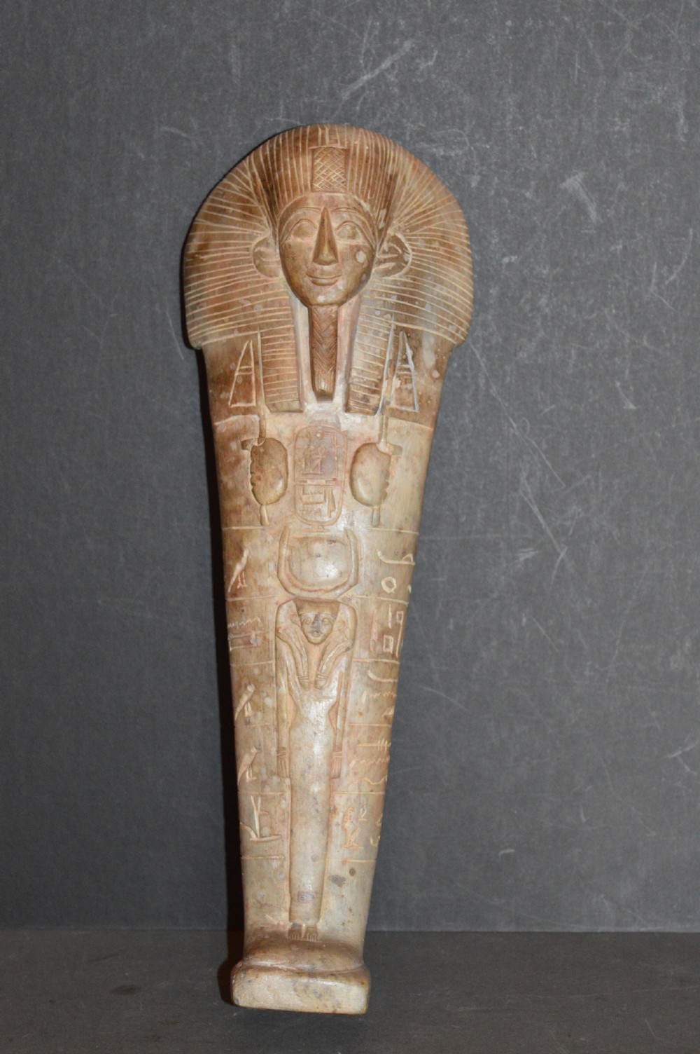 A carved beige stone model of an Egyptian sarcophagus lid featuring a pharaonic face with a nemes headdress and hieroglyphic engravings.