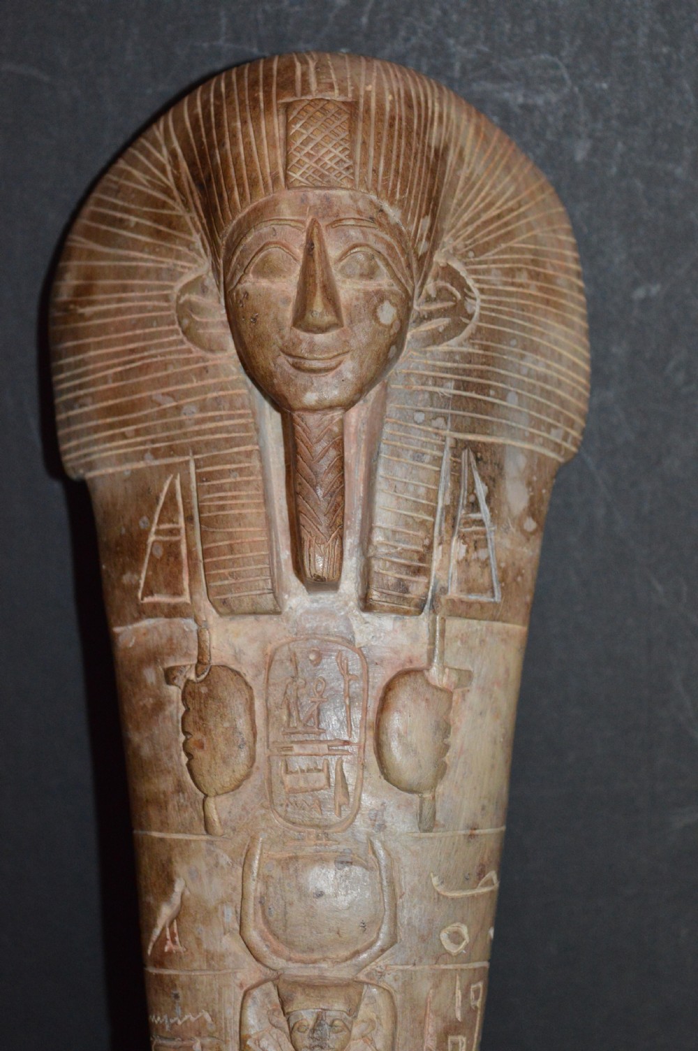 A carved beige stone model of an Egyptian sarcophagus lid featuring a pharaonic face with a nemes headdress and hieroglyphic engravings. View II