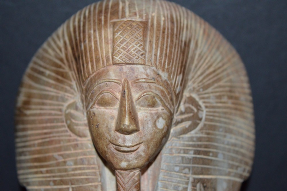 A carved beige stone model of an Egyptian sarcophagus lid featuring a pharaonic face with a nemes headdress and hieroglyphic engravings. View VI