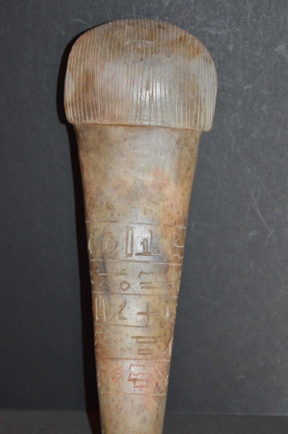 A carved beige stone model of an Egyptian sarcophagus lid featuring a pharaonic face with a nemes headdress and hieroglyphic engravings. View VIII