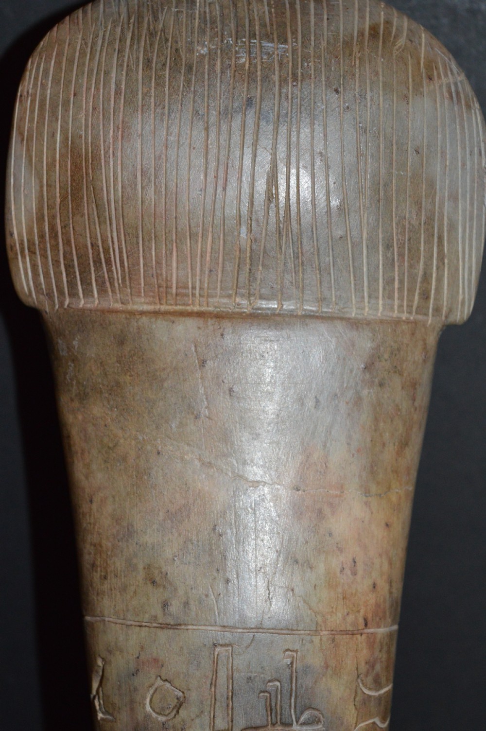 A carved beige stone model of an Egyptian sarcophagus lid featuring a pharaonic face with a nemes headdress and hieroglyphic engravings. View X