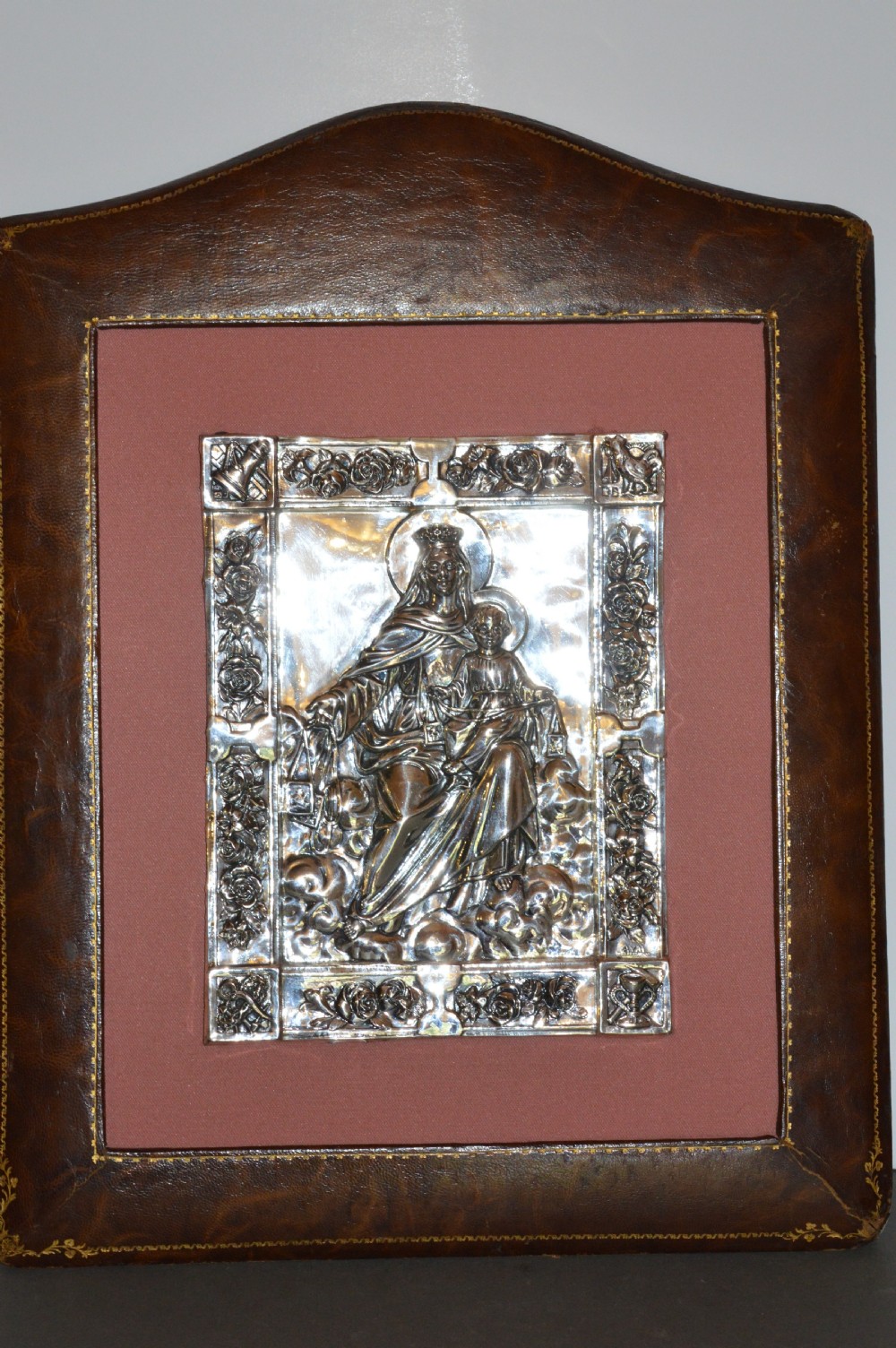 A 1920s Spanish religious icon depicting the Madonna and Child in embossed silver-toned metal, set within a brown leather frame. View II