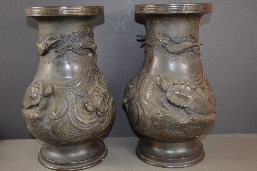 A pair of dark patinated Japanese bronze vases featuring high-relief carvings of flying birds and long-tailed turtles amongst stylised water waves.