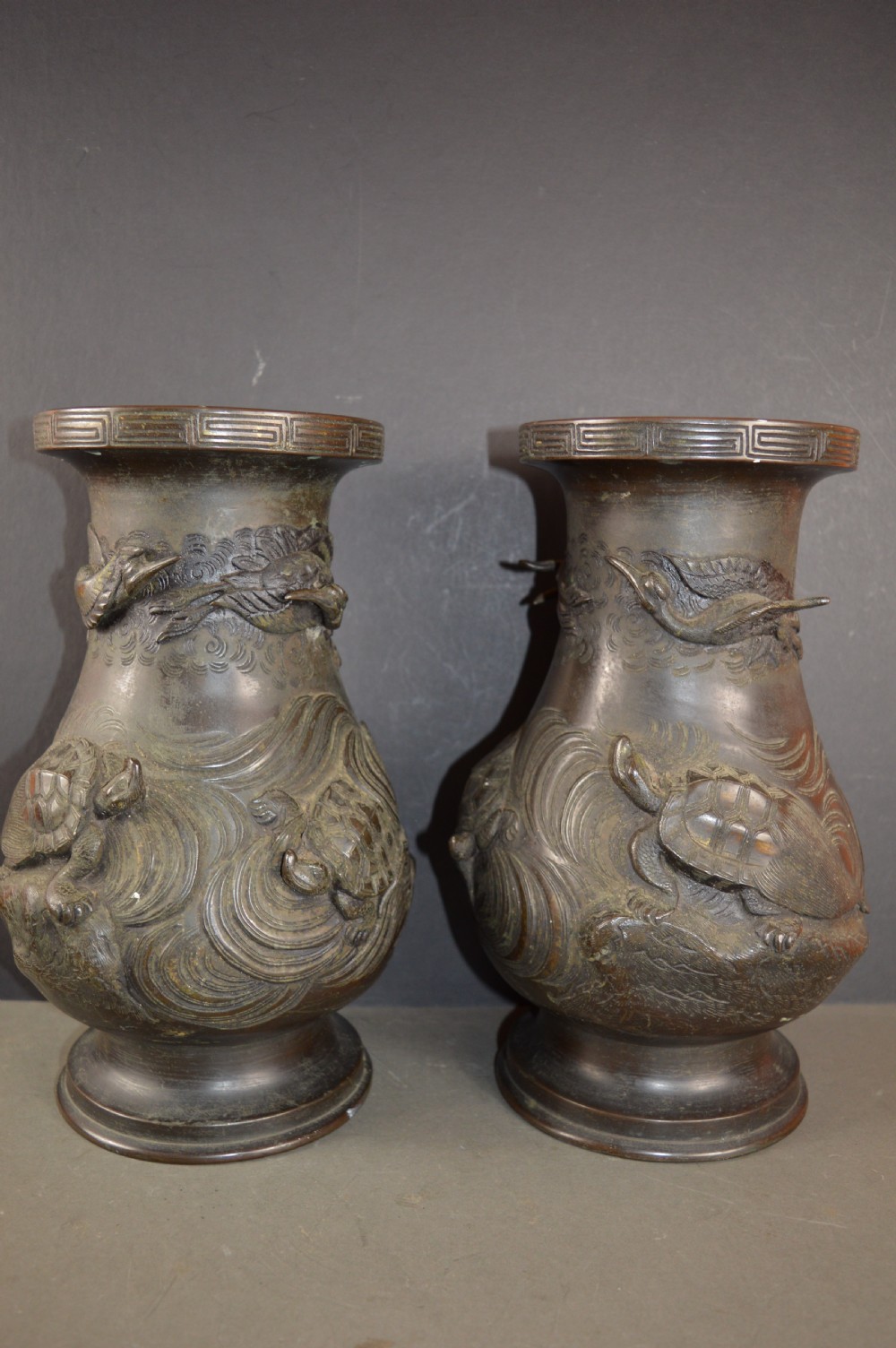 A pair of dark patinated Japanese bronze vases featuring high-relief carvings of flying birds and long-tailed turtles amongst stylised water waves. View II