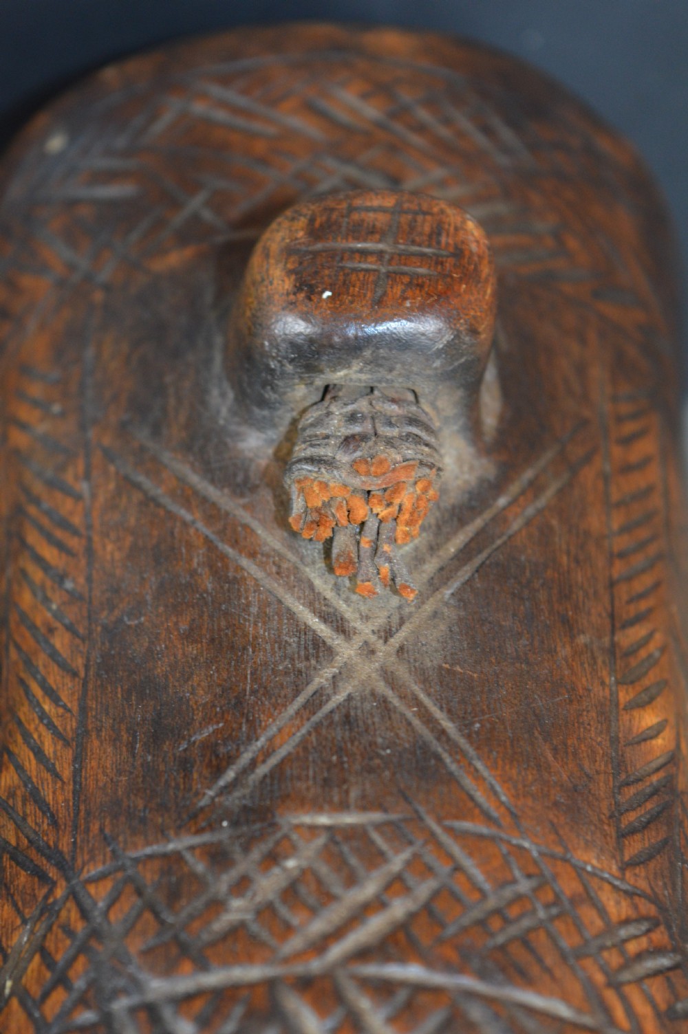 A cylindrical hand-carved dark wood vessel featuring geometric chevron patterns, side hanging lugs with fibre detail, and a flared pedestal base. View VII