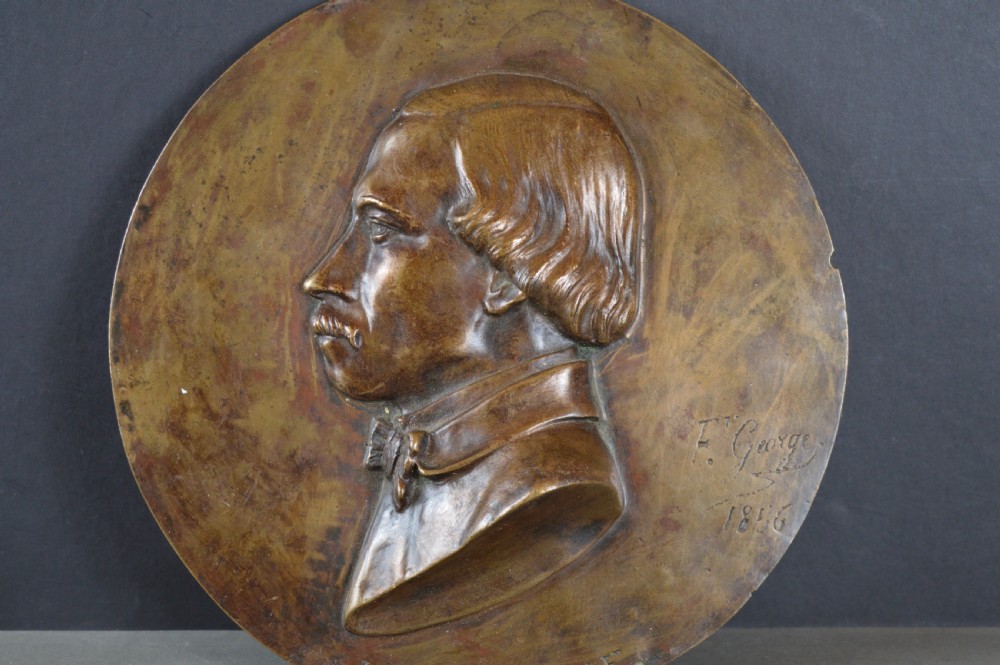 A circular patinated bronze relief plaque displaying a left-facing profile portrait of a man with a moustache, high collar, and bowtie, inscribed F George 1856.