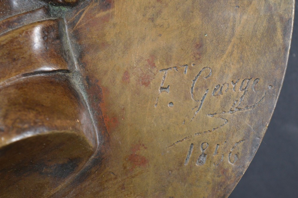 A circular patinated bronze relief plaque displaying a left-facing profile portrait of a man with a moustache, high collar, and bowtie, inscribed F George 1856. View V