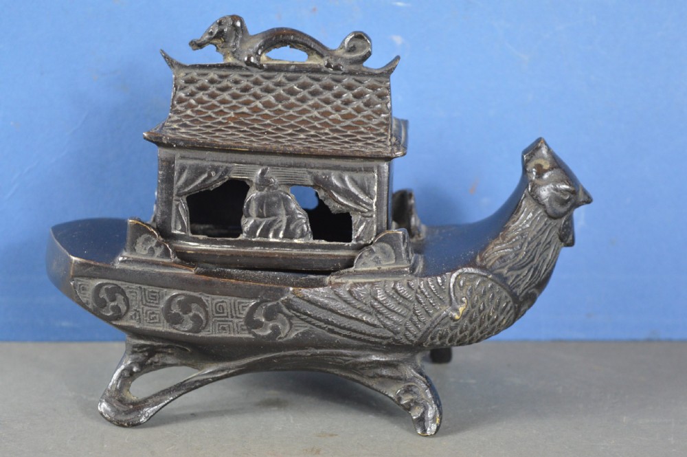 A dark patinated bronze Chinese censer cast in the form of a junk boat featuring a pagoda cabin, figure, and bird prow.